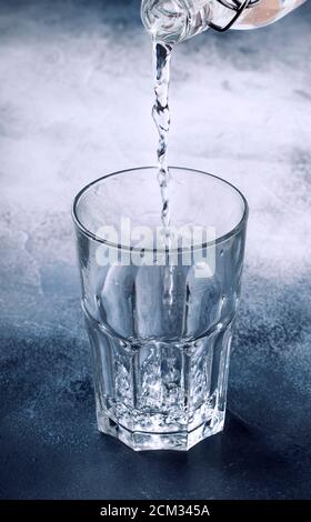 Clear water is poured from glass bottle into glass, gray background, selective focus Stock Photo