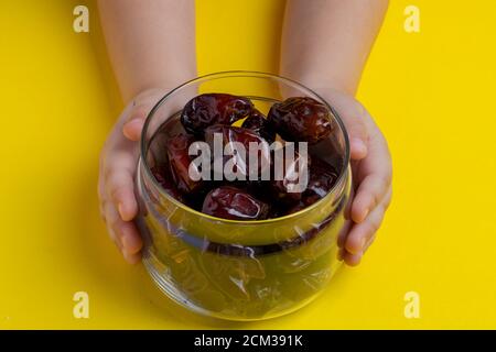 Hands holding dates in glass bowl on yellow background Stock Photo