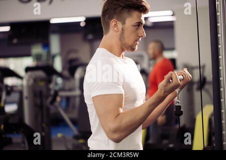 Handsome young guy pumping up upper body muscles doing exercises on gym mashine, workout bodybuilding concept Stock Photo