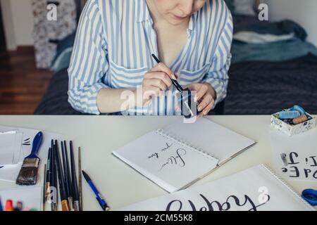 Close up of Female hand dipping calligraphy pen into inkwell Stock Photo