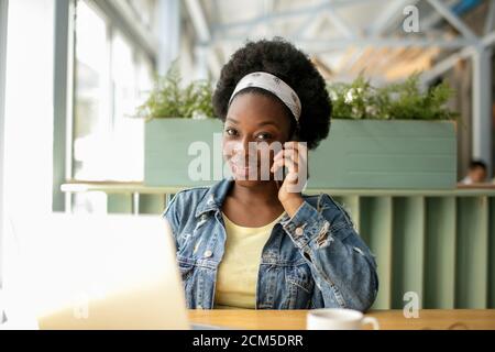 Keeping business on top with digital technologies. Cheerful young African american business lady, talking on smartphone and looking at digital tablet Stock Photo