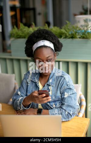 Keeping business on top with digital technologies. Cheerful young African american business lady, talking on smartphone and looking at digital tablet Stock Photo