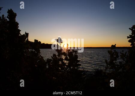 Sun setting over Belmont Bay with silhouette of trees and cliff Stock Photo