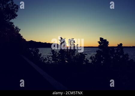 Sun setting over Belmont Bay with silhouette of trees and cliff Stock Photo