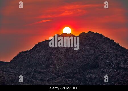 Close up of the sun setting over a mountain with swirling clouds and colorful sky Stock Photo