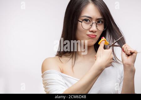 Discontent Asian girl having trouble with long hair, cutting the split ends off. Hare Care Stock Photo