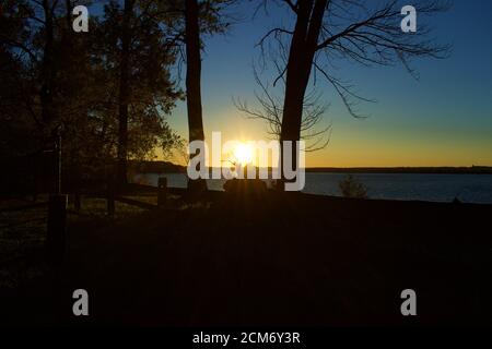 Sun setting over Belmont Bay with the silhouette of trees and cliff Stock Photo