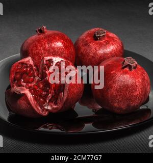 Pomegranate fruit laid out on a black plate, on a neutral gray fone Stock Photo