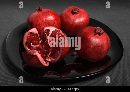 Pomegranate fruit laid out on a black plate, on a neutral gray fone, horizontal Stock Photo