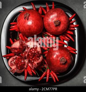 Pomegranate fruit laid out on a black plate, on a neutral gray background, view from above, top view Stock Photo