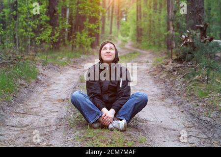 Man in the forest. A middle-aged woman sits on a forest road. Stock Photo