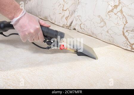 Dry cleaner's man employee removing dirt from furniture in flat, closeup, vacuum clean sofa with professional equipment Stock Photo