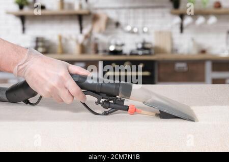 Dry cleaner's man employee removing dirt from furniture in flat, closeup, vacuum clean sofa with professional equipment Stock Photo