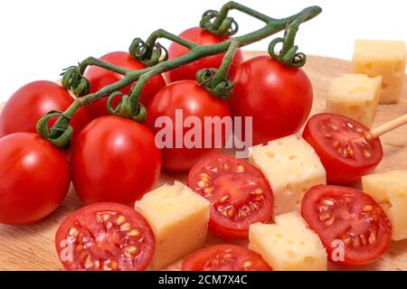piece of cheese and cheese skewers with tomato on a wooden board, cheese samples, cheese with holes cutout on white background Stock Photo