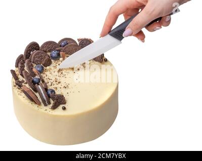 delicious and beautiful cake for a family bakery, with chocolate cookies and berries decoration. Hand with knife cuts a cake. isolated on white backgr Stock Photo