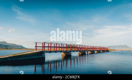 Red Bridge running over lagoon to beach, clear sunny day Stock Photo