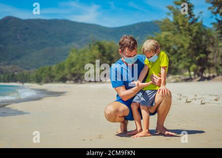 Father squatting holding son looking on open hand, play compare their palms, wearing face blue mask protect coronavirus walking nature sand sea beach Stock Photo