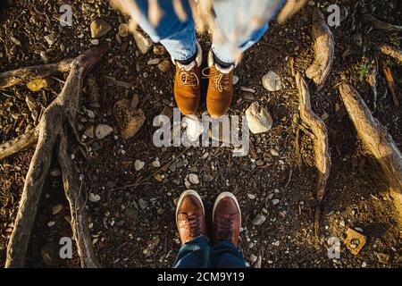 Male and female legs in brown boots in the roots of trees in the sunlight. View from above, flat composition. Family, date, relationship concept. Stock Photo