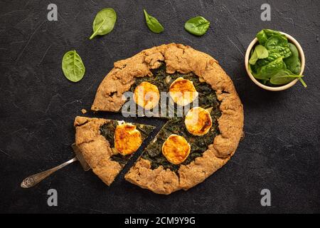 Rustic spinach and goat cheese galette on black background. Stock Photo