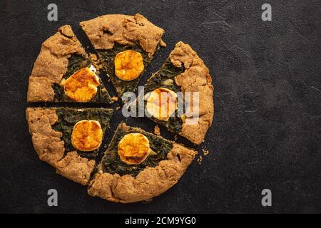 Rustic spinach and goat cheese galette on black background. Stock Photo