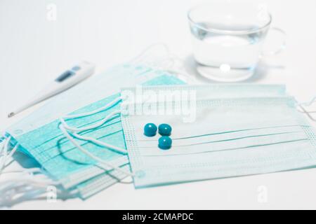 A medical mask to prevent the spread of the COVID-19 virus, three blue tablets and a thermometer with a glass Cup of water. Antiviral disposable face Stock Photo