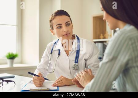 Positive doctor therapist sitting and listening to complaints of woman patient during consultation in medical clinic Stock Photo
