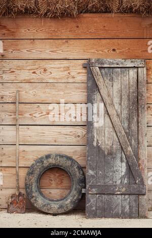 Old barn door, dirty old tire and shovel leaning against the wooden barn door on a farm Stock Photo