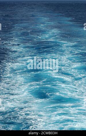 Frothy wakes created by a small boat trace on the water surface, vertical background, close-up shot with copy space, marine and environmental patterns Stock Photo