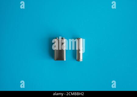 High voltage Volt 9V battery and alkaline AA battery on a blue background. Energy. Stock Photo