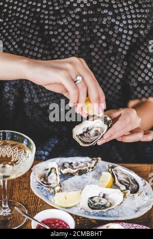 Woman squeezing lemon juice to fresh Irish oysters in restaurant Stock Photo