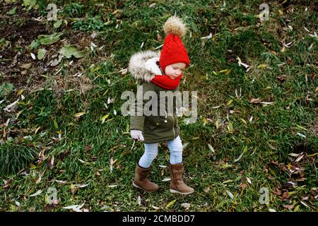 Cute little funny girl in trendy outfit walking outdoors in fall park, children fashion, full body portrait Stock Photo