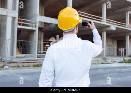 Builder Taking Photos by Phone of Cunstruction Works. Man in Hardhat. House Building Stock Photo