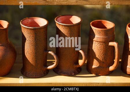 brown clay mugs stand in rows on a wooden shelf. Stock Photo