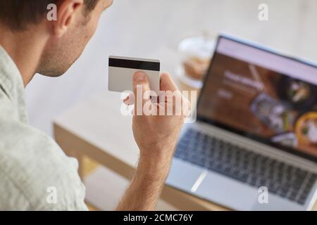 Rear view of man holding credit card and paying for food delivery online using laptop Stock Photo
