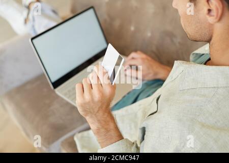 Close-up of young man holding credit card and paying online for purchases using laptop computer Stock Photo