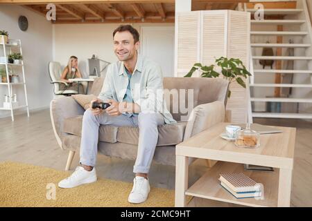Young happy man sitting on sofa and playing in computer games during his leisure time at home Stock Photo