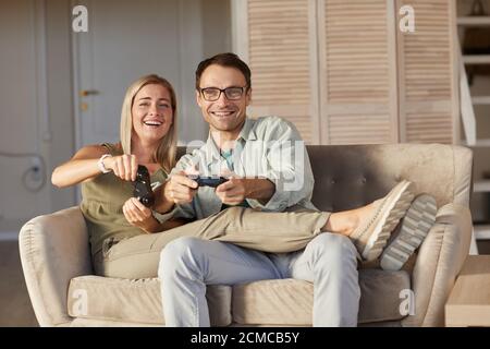 Portrait of young couple smiling at camera while having fun during play in computer games at home Stock Photo