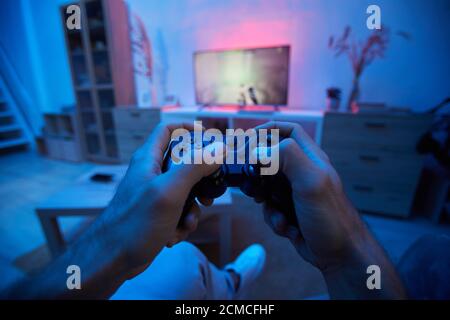 Close-up of man pushing buttons on joystick during video game on TV in dark living room at home Stock Photo
