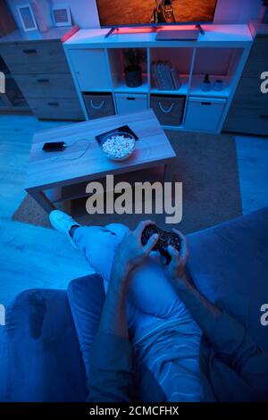 High angle view of gamer using joystick during video game in dark living room Stock Photo