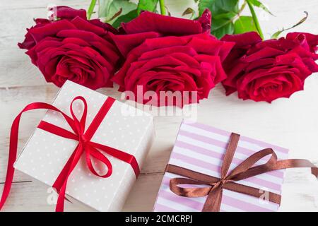 two gift boxes with ribbon bow and bautiful red roses on wooden background. Greeting card for holiday. Stock Photo