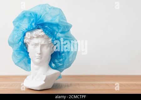 Gypsum copy of David's head in surgical cap. Michelangelo's David plaster bust, ancient sculpture, statue on wooden table. Medicine concept, operation Stock Photo