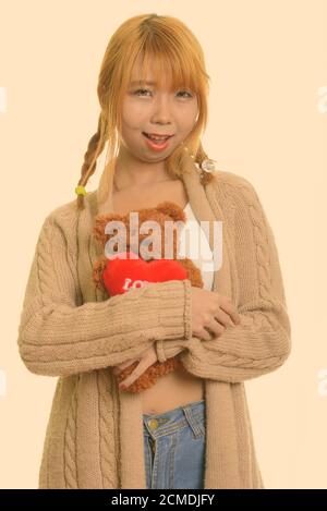 Young happy Asian woman smiling and hugging teddy bear with heart and love sign Stock Photo