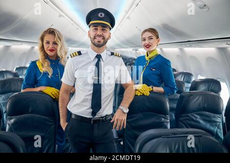 Happy smiling handsome pilot with two air hostess on the board of plane Stock Photo