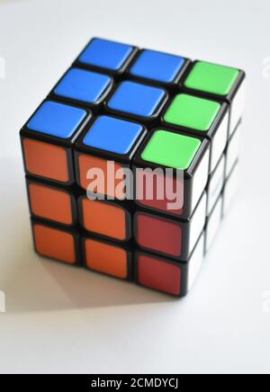 An isolated Rubik's Cube puzzle sits almost solved on a crisp white background in bright natural light Stock Photo