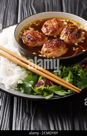 Bun cha consists of rice vermicelli noodles (bun), grilled pork (cha) and a type of broth closeup in the plate on the table. Vertical Stock Photo