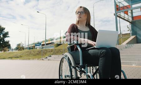 Young caucasian woman in the wheelchair using laptop. Train passing in the background. High quality photo Stock Photo