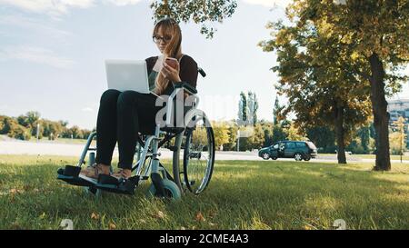 Remote work concept. Young disabled woman in the wheelchair using smartphone and laptop. High quality photo Stock Photo