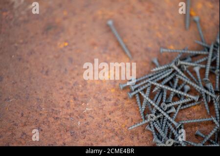 Black self-tapping screws scattered on a rusty sheet of metal, close-up, selective focus Stock Photo
