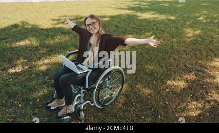 happy young disabled caucasian woman in the wheelchair resting in the nature with laptop and smartphone . High quality photo Stock Photo