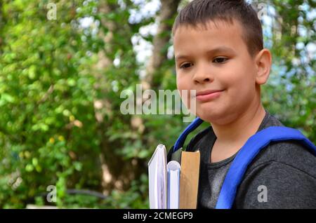 smiling schoolboy looking at camera while standing in park and holding books Stock Photo